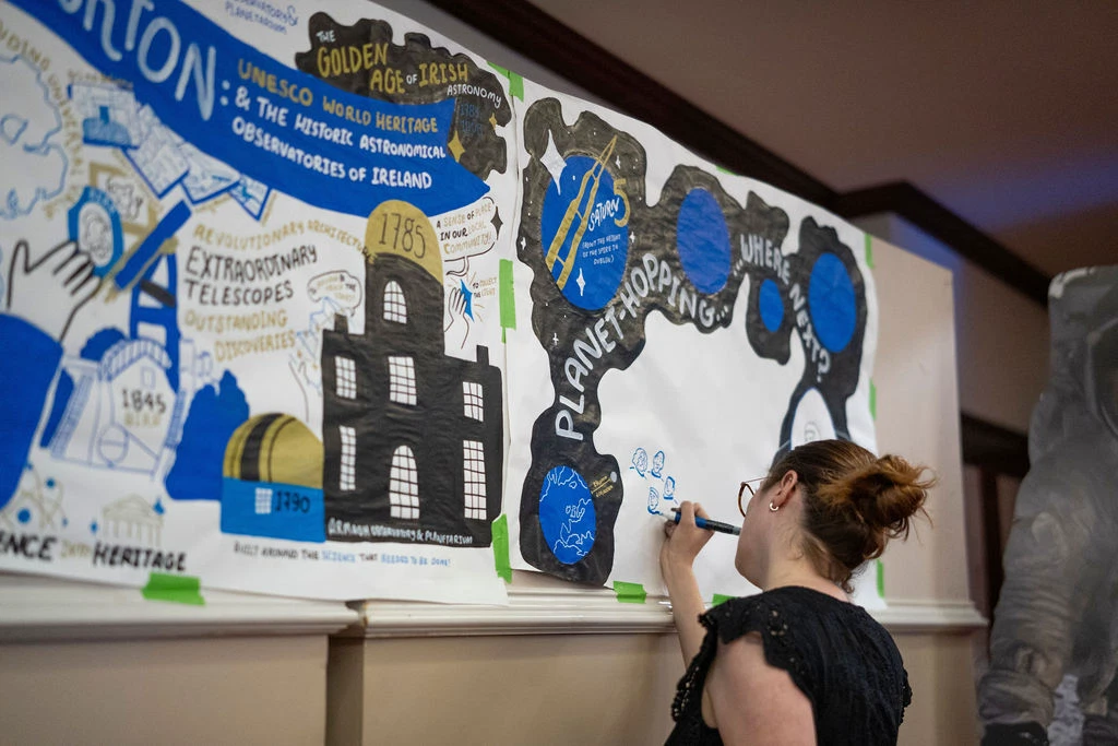 Artist illustrating astronomy-themed mural at Mayo Dark Sky Festival event.