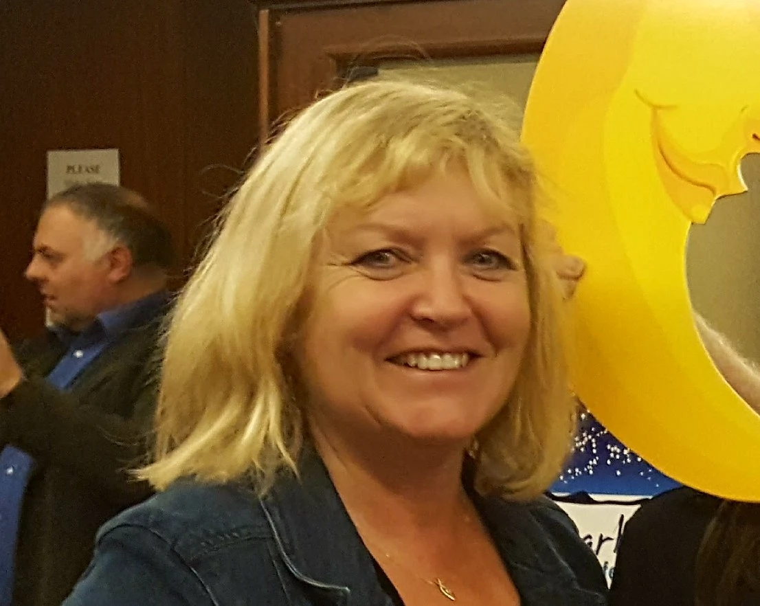 Blonde woman smiling at Mayo Dark Sky Festival, standing by yellow crescent moon decor indoors.