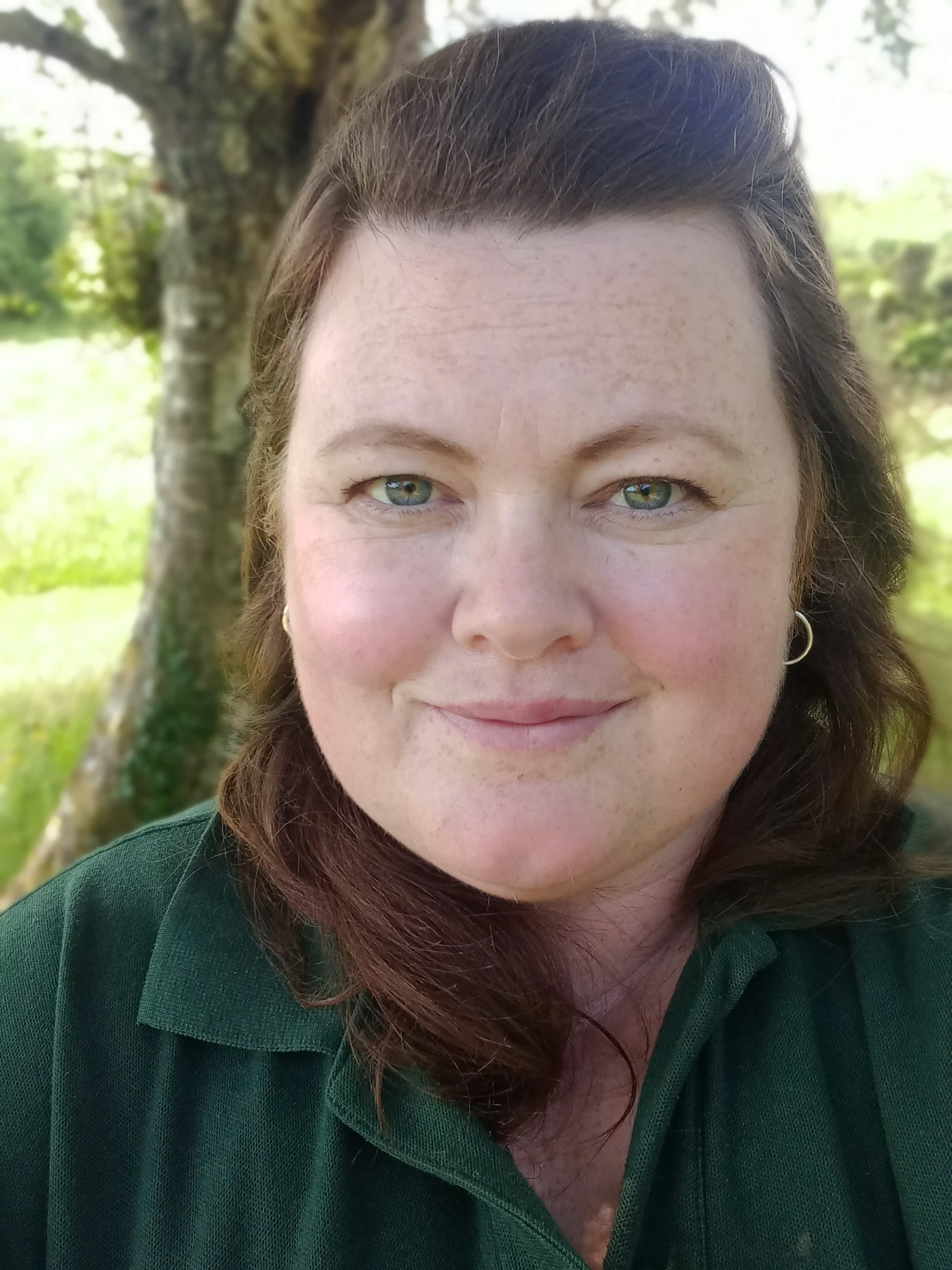 Portrait of a smiling individual outdoors, set against a backdrop of greenery and a tree at the Mayo Dark Sky Festival.