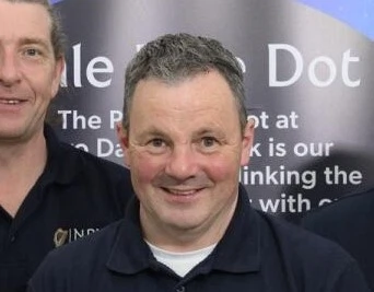 Man smiling in front of Mayo Dark Sky Festival banner, wearing a navy shirt, at a star-gazing event in Ireland.