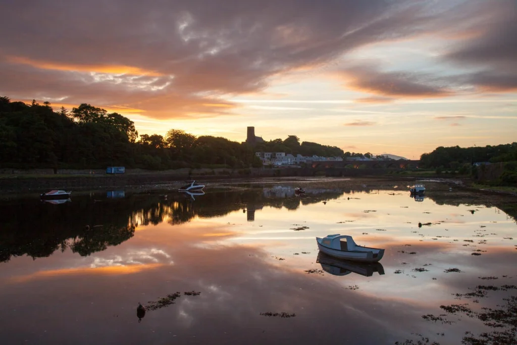 Serene evening at Mayo Dark Sky Festival with boats reflecting on calm water under a vibrant sunset.