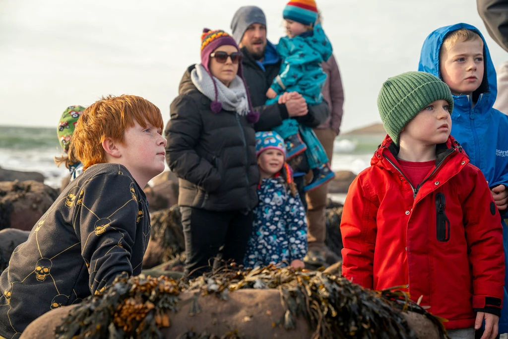 Families exploring the rocky Mayo coastline during the Dark Sky Festival under a cloudy sky.